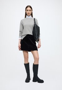 Szürke pulóver fehér garbóval, fekete kordnadrág szoknya és magas fekete gumicsizma. Fekete táska ívelt dizájnnal és állítható pánttal.