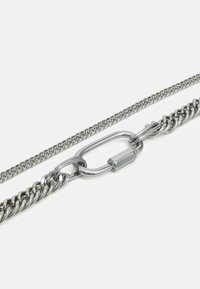 Colar de corrente metálica com duas correntes entrelaçadas: uma com design plano e a outra com anéis entrelaçados, ambas com acabamento prateado polido.