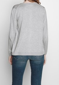 Grå långärmad tröja med rundad halsringning, med texturerade axelaccenter och en avslappnad passform. Matchas med mörka denimjeans.