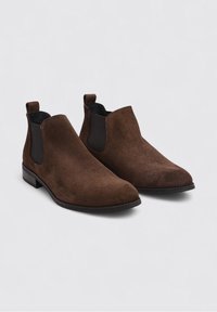 Bottines en suede marron avec panneaux latéraux en élasthanne et languettes de tirage. Texture lisse, bout rond et petit talon bloc. Design simple et accents sombres.