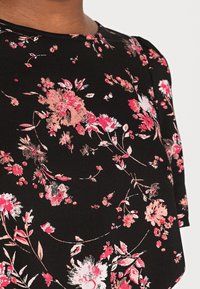 Top nero floreale con motivi di fiori rosa e bianchi, maniche corte e scollatura rotonda. Il tessuto appare liscio con una leggera lucentezza.