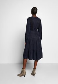 Mörkblå klänning med långa ärmar, lager-på-lager kjol och texturerade svarta detaljer på bysten. Kombinerad med spetsiga ankelskor i ormskinnsmönster.