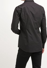 Zwart shirt met lange mouwen en een kraag, nauwsluitende achterkant, gladde stof en subtiele glans. Draagt het met een donkere broek.