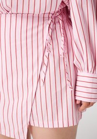 Robe enveloppante rose et blanche à rayures en tissu léger, dotée d'une fermeture à nouer, de manches longues et d'un ourlet décontracté avec des poignets.