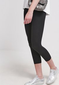 Leggings capri negros hechos de material elástico, con un diseño ajustado que termina justo debajo de la rodilla, combinados con zapatillas plateadas y un bolso con lentejuelas.