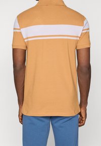 Musztardowa koszulka polo w białe poziome paski, z krótkimi rękawami i kołnierzykiem; fakturowana tkanina, standardowy krój.