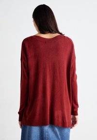 Bordeaux gebreide trui met een losse pasvorm, verlaagde schouders, ribgebreide manchetten en zoom. Zachte textuur, gedragen met een denim rok.