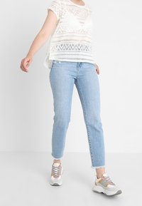 Bílý vzorovaný top s krátkými rukávy, světle modré džíny s roztrhanými lemy a barevné chunky tenisky. Jednoduchý design a ležérní styl.