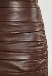 Bruine leren rok met geplooide textuur en een gladde afwerking. Kenmerkt zich door horizontale plooien en stikdetails.