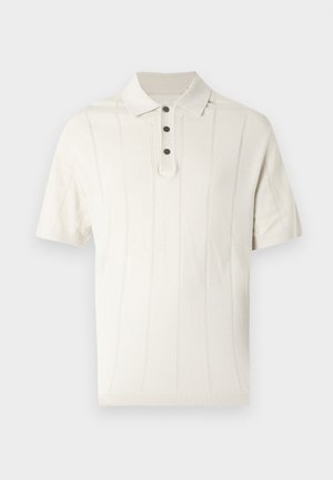 Κρεμ κοντομάνικη πόλο μπλούζα με τρία μαύρα κουμπιά και διακριτικές κάθετες ριγέ λεπτομέρειες πλέξης σε απλό φόντο.