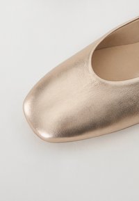 Scarpa piatta in oro rosa metallico con punta arrotondata, tessuto in pelle liscia e design a taglio basso, caratterizzata da una leggera lucentezza.