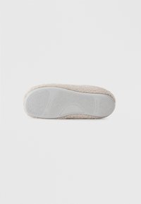 Zachte beige slipper onderkant met textuur en pluizig materiaal. Witte rubberen loopzool heeft een patroon voor grip en een gebogen ontwerp voor comfort.