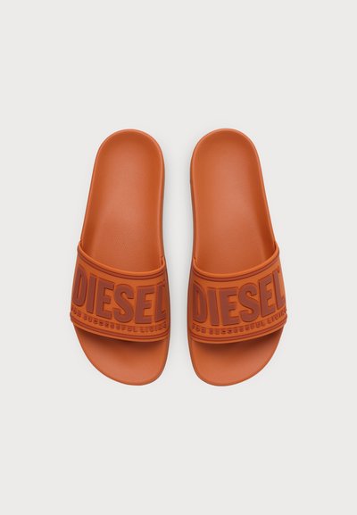 Двойка оранжеви слайд сандали Diesel с релефни ленти с лого на обикновен бял фон.