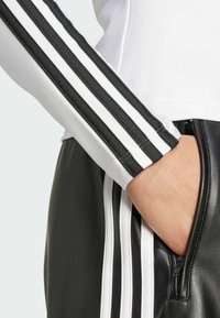 Mustat nahkahousut, joissa on valkoiset sivustripit, sekä valkoinen paita, jossa on mustat raidat hihoissa. Materiaali näyttää sileältä ja istuvalta.