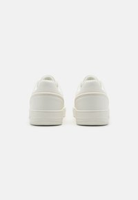 Bílé tenisky s hladkým koženým svrškem, polstrovaným límcem a texturovanou gumovou podrážkou. Minimalistický design s nenápadnými švy.