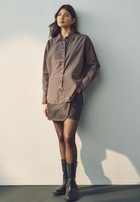 Brown button-up shirt made of lightweight fabric, paired with a dark denim skirt and knee-high black leather boots. Smooth texture with a relaxed fit.