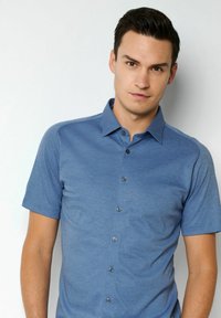 Kurzärmliges Hemd mit Knopfleiste aus einfarbigem blauen Stoff. Verfügt über einen spitzen Kragen und ein dezentes Texturmuster mit fünf schwarzen Knöpfen vorne.