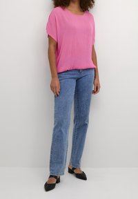 Fuchsiastråle, løs pasform toppen med korte ærmer, parret med lyseblå lige ben jeans og sorte spidse sko. Glat tekstur.