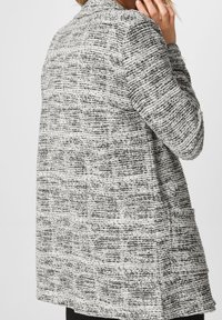 Cardigan long texturé en noir et blanc, doté d'un col, de manches longues et d'une ouverture sur le devant. Remarquable pour son motif tissé et sa coupe décontractée.