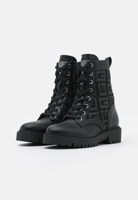 Bottes de combat noires avec une tige en tissu texturé, présentant un motif de logo. La semelle est épaisse avec un design cranté pour une meilleure adhérence.