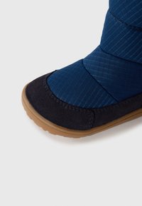Botine din suede bleumarin cu textile albastre, cu un superior texturat, talpă plată din cauciuc și vârf rotund. Prezintă margini cusute și dungi diagonale.