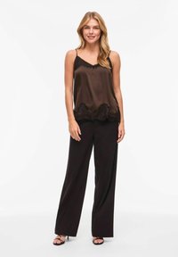 Camisole en satin marron avec bordure en dentelle noire à l'ourlet, associée à un pantalon noir taille haute, portée avec des talons noirs à brides.