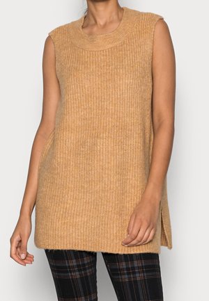 Pull sans manches en tricot de couleur brun clair avec des côtes verticales, des fentes sur les côtés et un col rond, associé à un pantalon à carreaux.