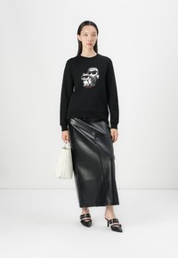 Felpa nera con una stampa grafica di due personaggi dei cartoni animati. Abbinata a una lunga gonna di pelle nera, borsa bianca e scarpe nere con tacco.