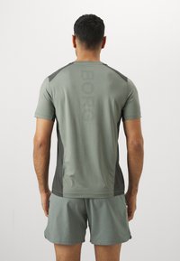 Camisola atlética verde-claro de mangas curtas, com detalhes pretos nos ombros e o logótipo pontilhado "BORG" na parte de trás. Combinada com calções a condizer.