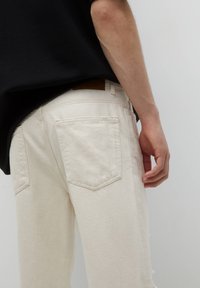 Beiget väriset farkut, joissa on hieman väljempi istuvuus, kaksi takataskua ja nahkainen merkintä vyötäröllä. Pintakuvioitu kangas näkyvin saumin.