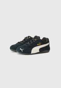 Black and white Puma sneakers with a suede finish, featuring a gold logo on the tongue and contrasting white swoosh design on the side.