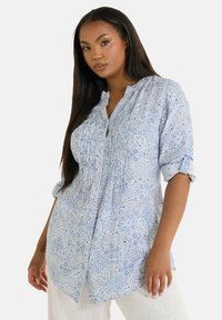Camicia azzurro chiaro con motivo paisley, dotata di colletto abbottonato, dettagli arricciati e maniche arrotolate, realizzata in un tessuto morbido e texturizzato.