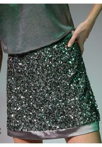 Jupe à paillettes avec une surface grise argentée brillante, ornée de paillettes noires et argentées, et finie par un ourlet en satin lisse.