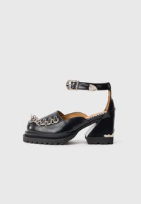 Pantofi platform negri din piele cu curea la glezna, detaliu din lanț argintiu în față și un design unic al tocului. Talpă din cauciuc pentru aderență.