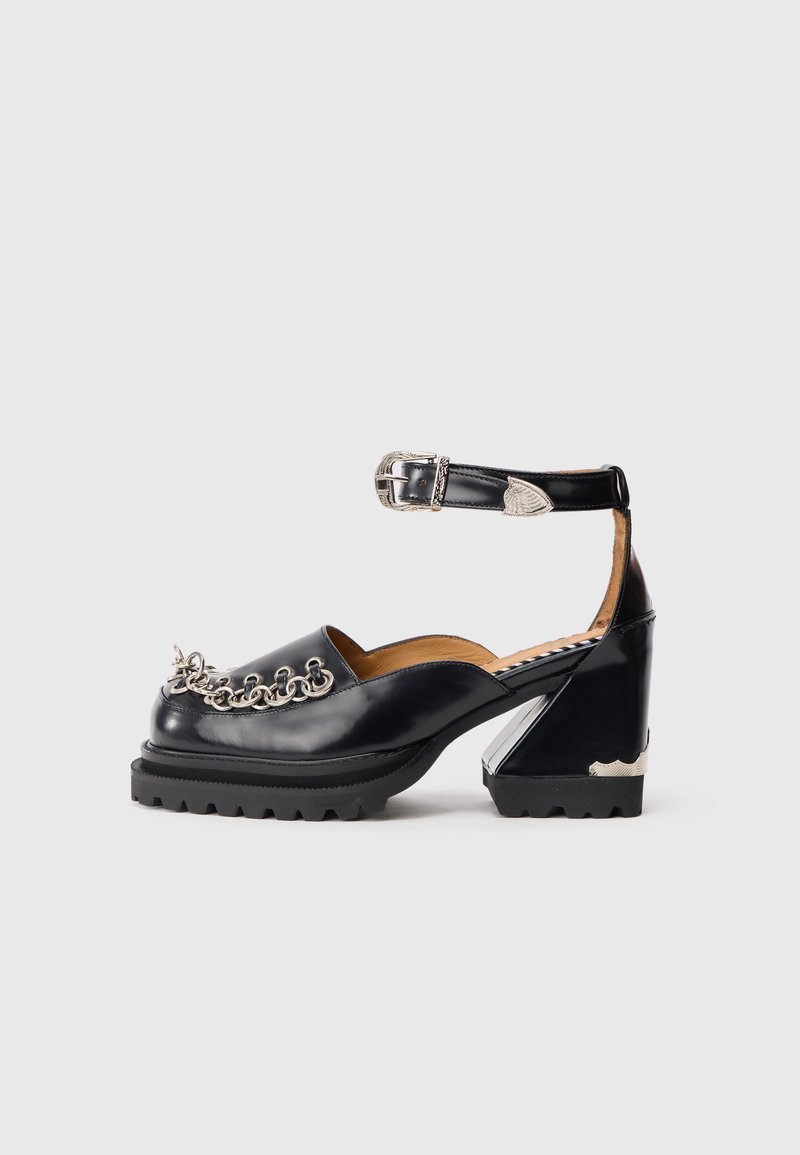 Pantofi platform negri din piele cu curea la glezna, detaliu din lanț argintiu în față și un design unic al tocului. Talpă din cauciuc pentru aderență.