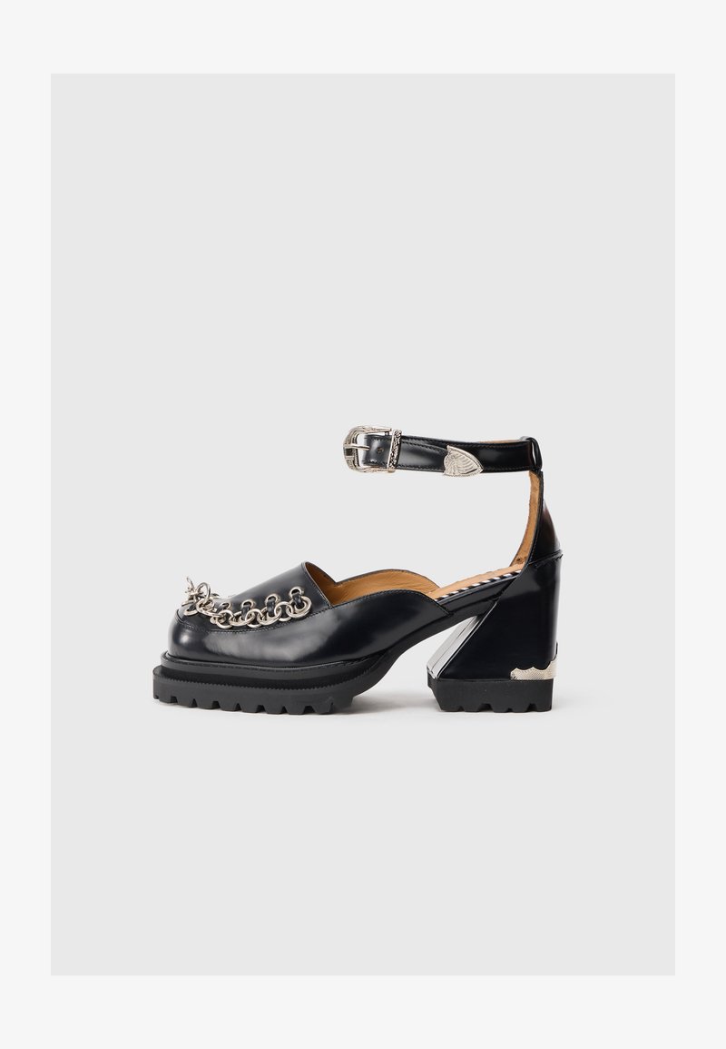 Pantofi platform negri din piele cu curea la glezna, detaliu din lanț argintiu în față și un design unic al tocului. Talpă din cauciuc pentru aderență.