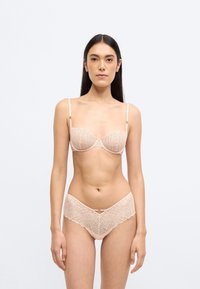 Σετ εσώρουχων σε μπεζ χρώμα με σουτιέν από δίχτυ με γεωμετρικά σχέδια δαντέλας και ταίριαστο σλιπ με κυματιστές άκρες. Περιλαμβάνονται ρυθμιζόμενοι ιμάντες.