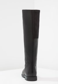 Bota negra hasta la rodilla hecha de cuero suave con un panel de ante en la parte posterior. Presenta una suela plana y punta redondeada.