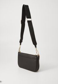 Mustat nahka crossbody -laukkua, jossa on karheapinta, kultaiset metalliosat ja musta brändätty olkahihna. Suorakulmainen muoto, vetoketjusulkunen.
