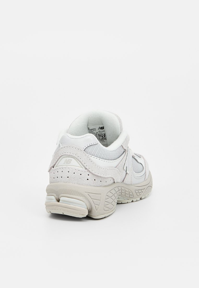 Zapatilla deportiva blanca con parte superior de malla texturizada, acentos de ante y talón acolchado. Presenta una suela acolchada y sutiles agujeros de ventilación.