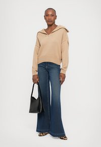 Beige gerippter Strickhoodie mit Reißverschluss, weiten Ärmeln, kombiniert mit weit geschnittenen dunkelblauen Jeans, einer schwarzen Handtasche und Schuhen mit Leopardenmuster.