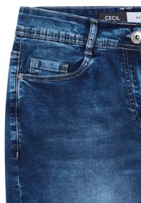 Jean en denim bleu avec poche avant et petite poche à monnaie, rivets métalliques, fermeture par bouton et étiquette de marque "Cecil" à l'intérieur de la ceinture.