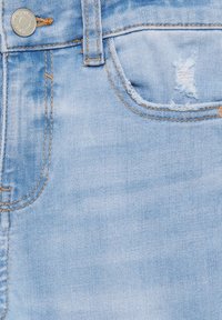 Tissu en denim bleu clair avec une petite déchirure usée sur la poche. Design classique à cinq poches avec surpiqûres contrastées et bouton en métal.