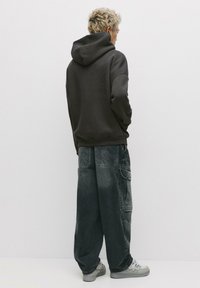 Felpa grigia scura con tasca a marsupio, abbinata a pantaloni cargo grigi sbiaditi e dalla vestibilità ampia. Presenta più tasche e dettagli di cucitura discreti.