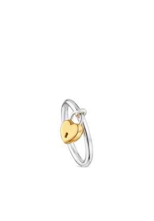 Anello in argento con un piccolo ciondolo a forma di lucchetto a forma di cuore dorato appeso alla sua fascetta su sfondo bianco.