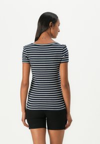 Ναυτικό μπλε ριγέ μπλούζα με λευκές ρίγες, εφαρμοστή γραμμή, κοντά μανίκια και στρογγυλή λαιμόκοψη, φορεμένη με μαύρη σορτς.