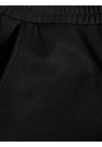 Black fabric close-up with a smooth texture, featuring a gathered waistband and a visible side seam. No patterns or additional details present.