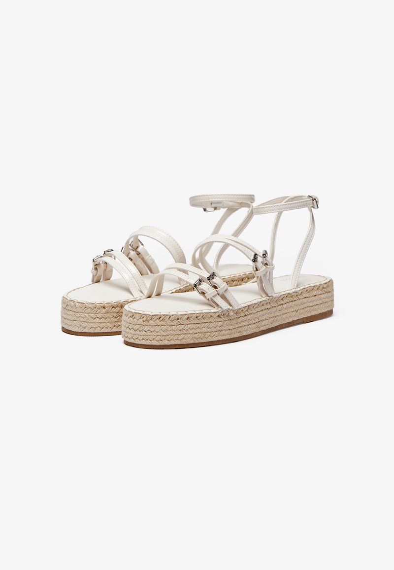 Sandalias de esparto de cuero blanco con múltiples correas, suela de yute trenzado y una plantilla texturizada. Cuenta con correas ajustables en el tobillo y acentos metálicos.