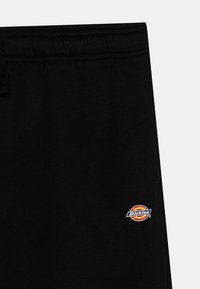 Black sweatpants featuring a drawstring waist and a small circular Dickies logo in red, yellow, and blue on the left side. Smooth texture.