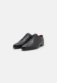 Scarpe in pelle nera con un motivo in rilievo a coccodrillo, caratterizzate da un design elegante, punta arrotondata e interno con accenti rossi.